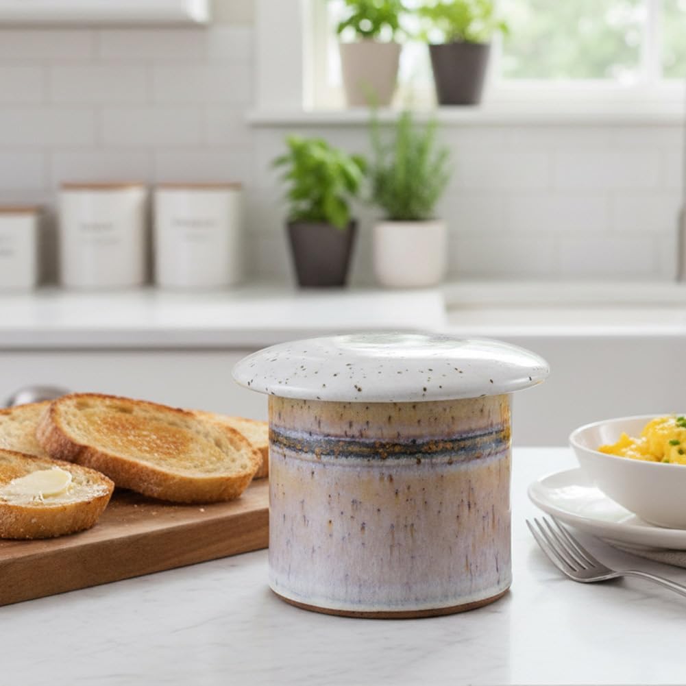 Ceramic butter dish on a kitchen counter with toast and a bowl of salad.