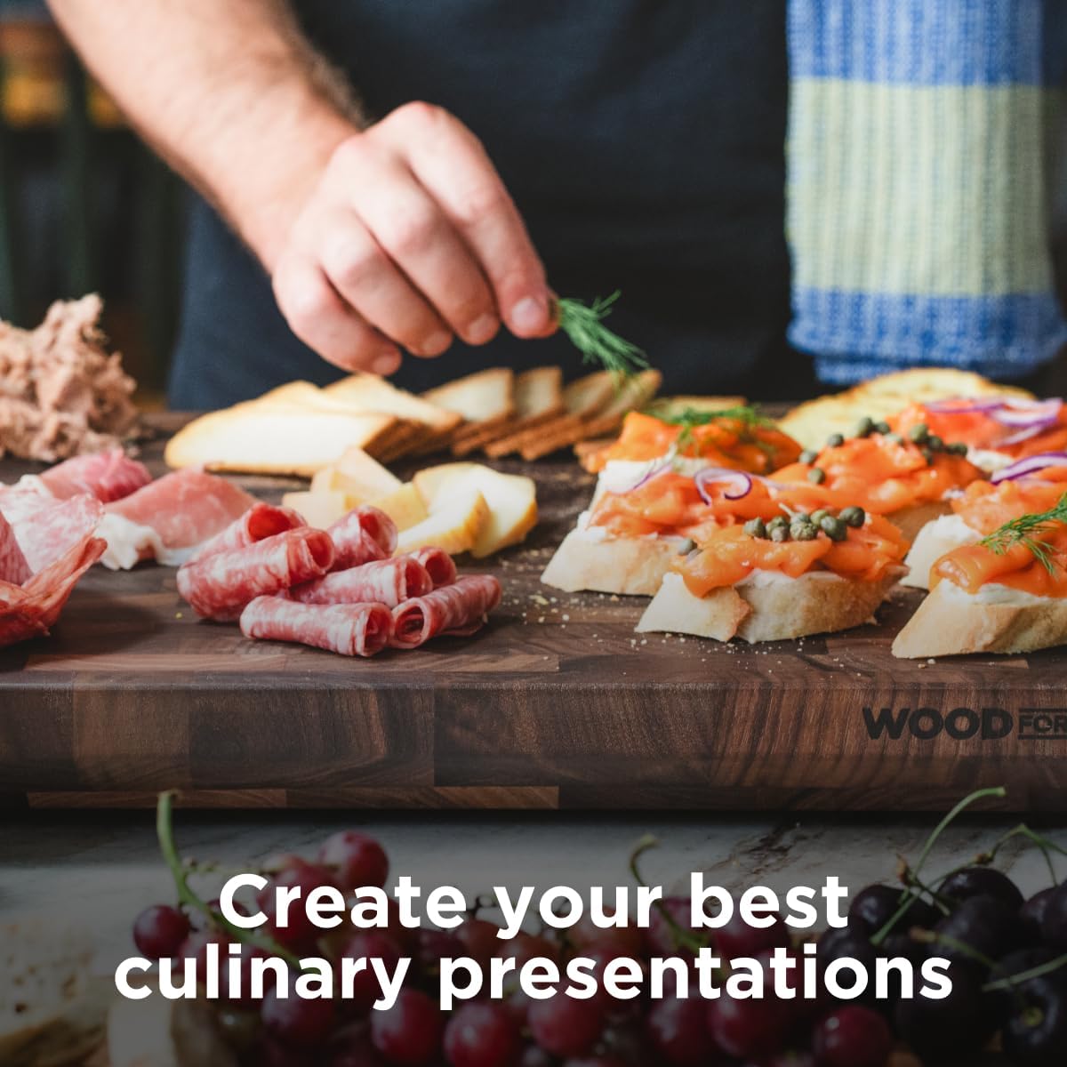 Person preparing a culinary display with cured meats, cheeses, and bread on a wooden board.
