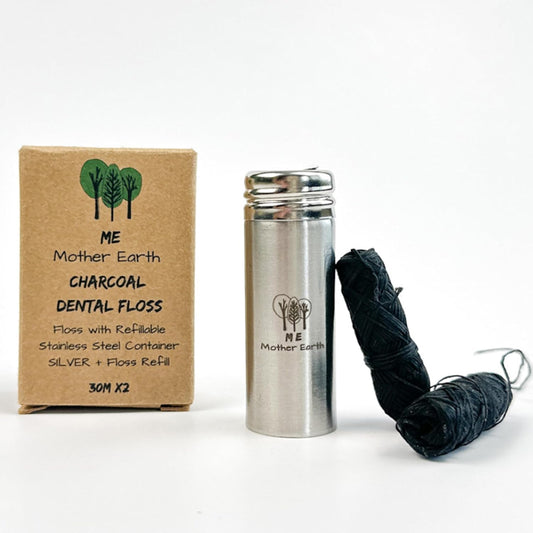 Charcoal dental floss set by ME Mother Earth, featuring a brown cardboard box, a silver stainless steel container, and two black wound-repairing charcoal floss wraps on a white background.