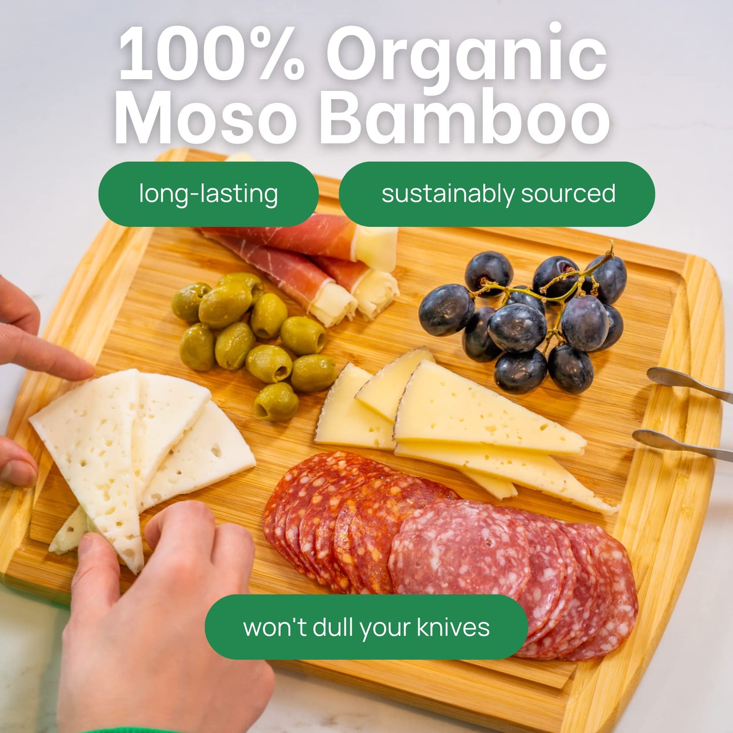 Wooden cutting board with cheese, salami, olives, and grapes, labeled '100% Organic Moso Bamboo'.