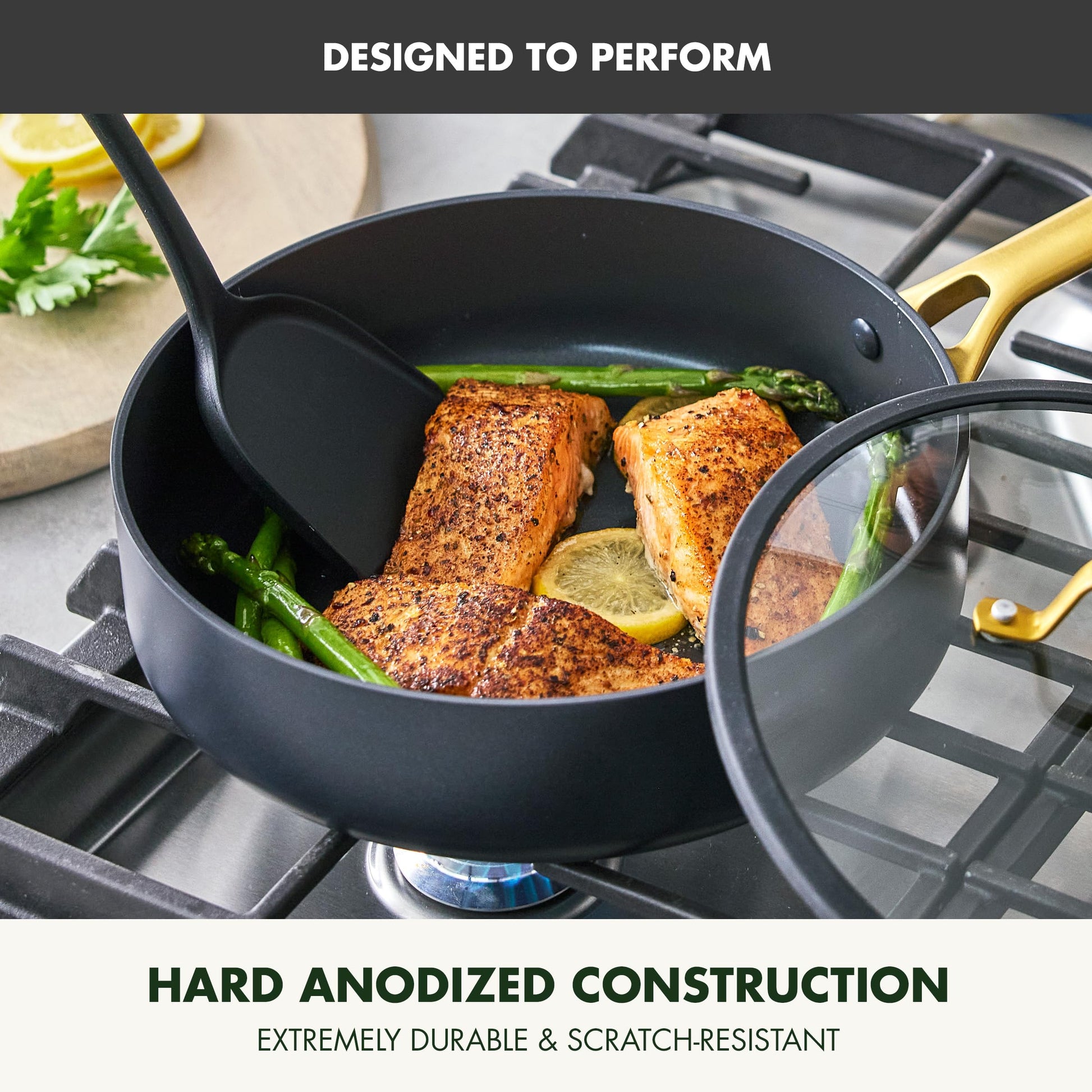 Black cookware set with salmon and vegetables on a stove, featuring hard anodized construction text.