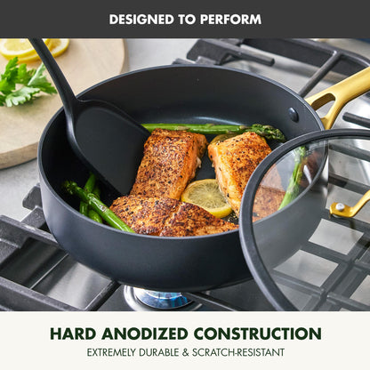 Black cookware set with salmon and vegetables on a stove, featuring hard anodized construction text.