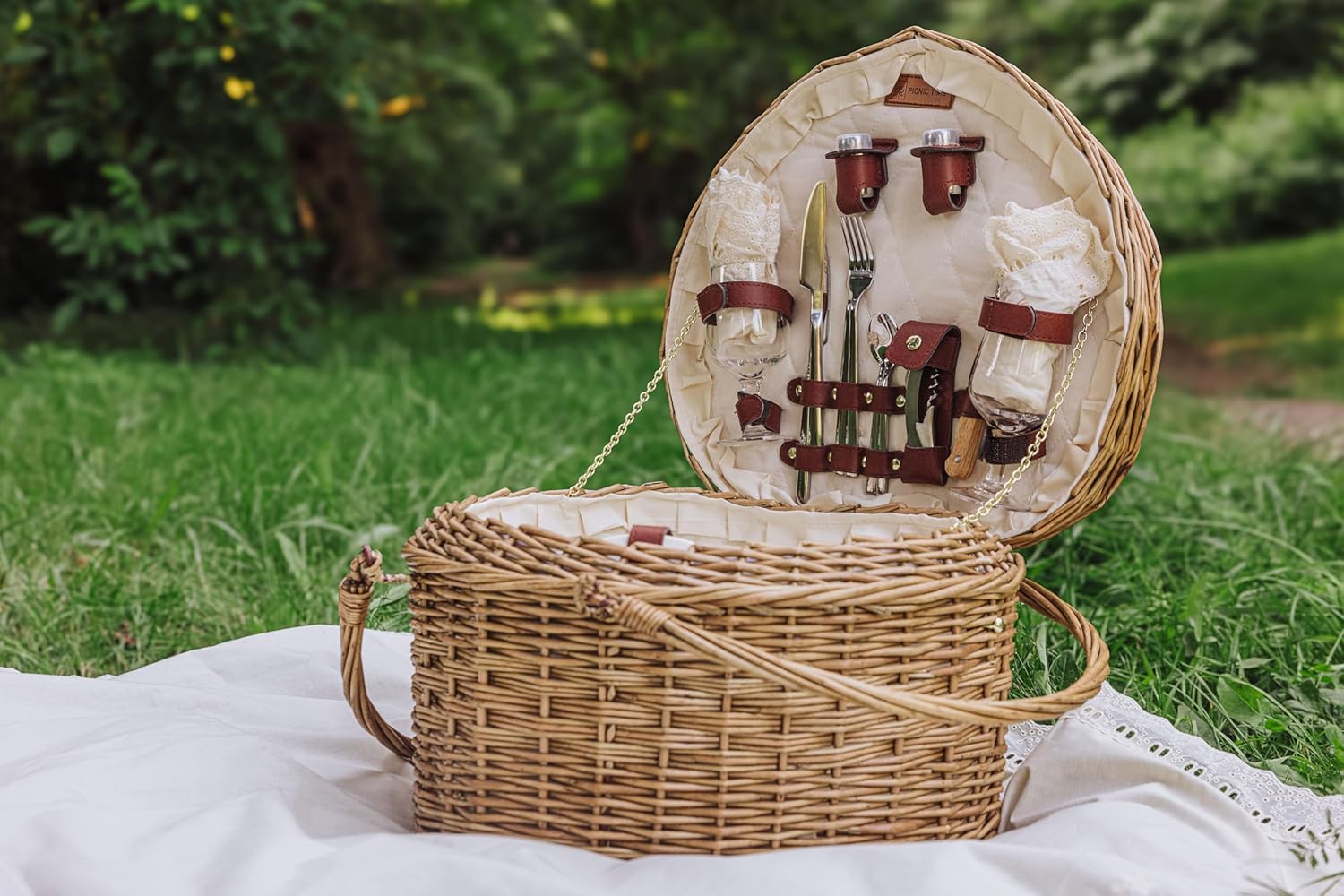 Wicker picnic basket with cutlery set on a blanket outdoors
