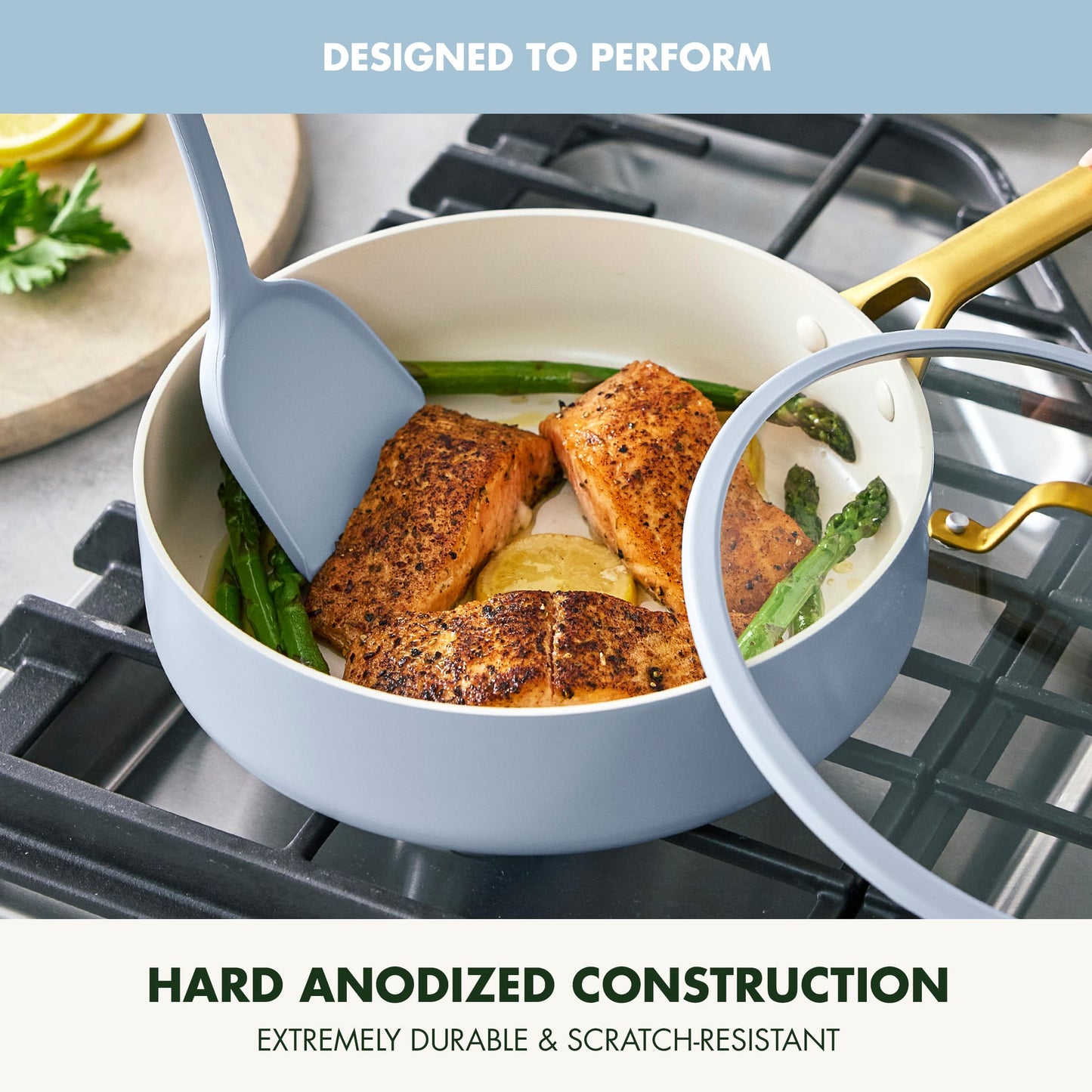 Cooking scene with a pot on a stove containing salmon and asparagus, with text about hard anodized construction.