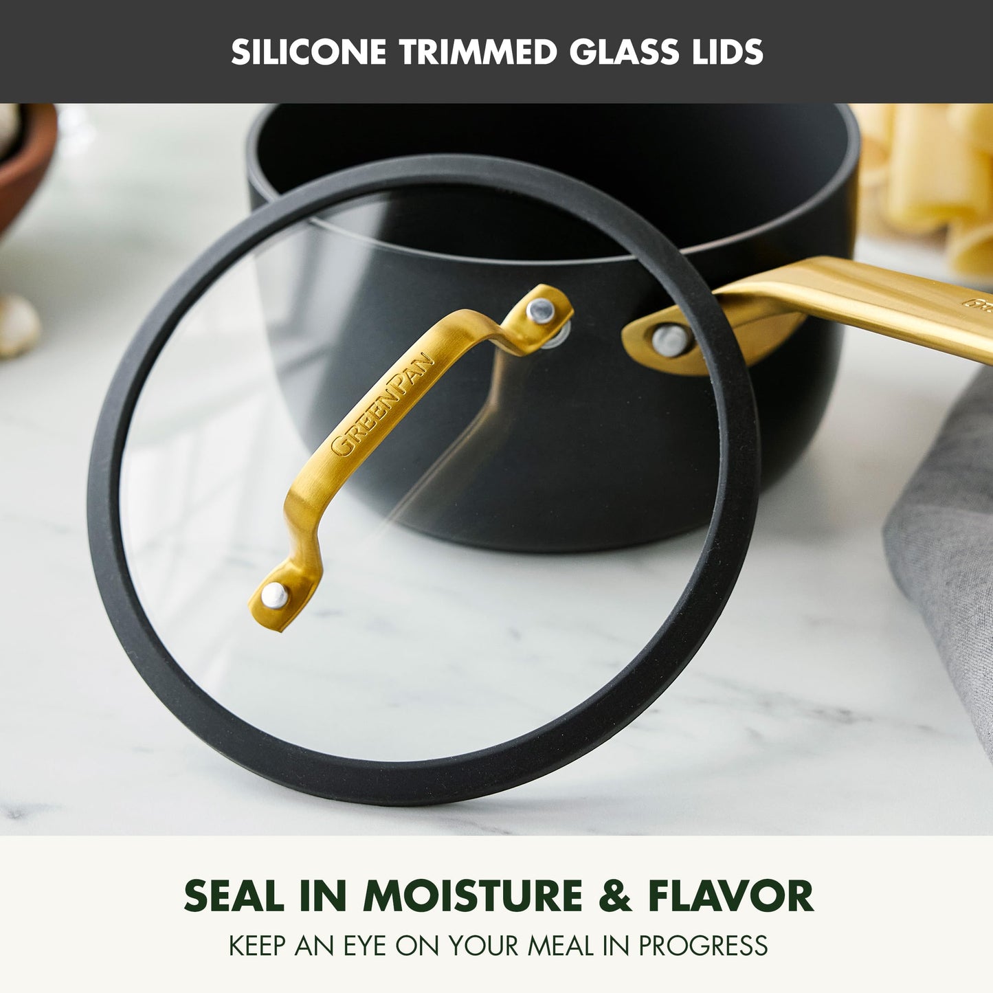 Glass lid with silicone trim on a pot, featuring gold handle, on a marble surface.