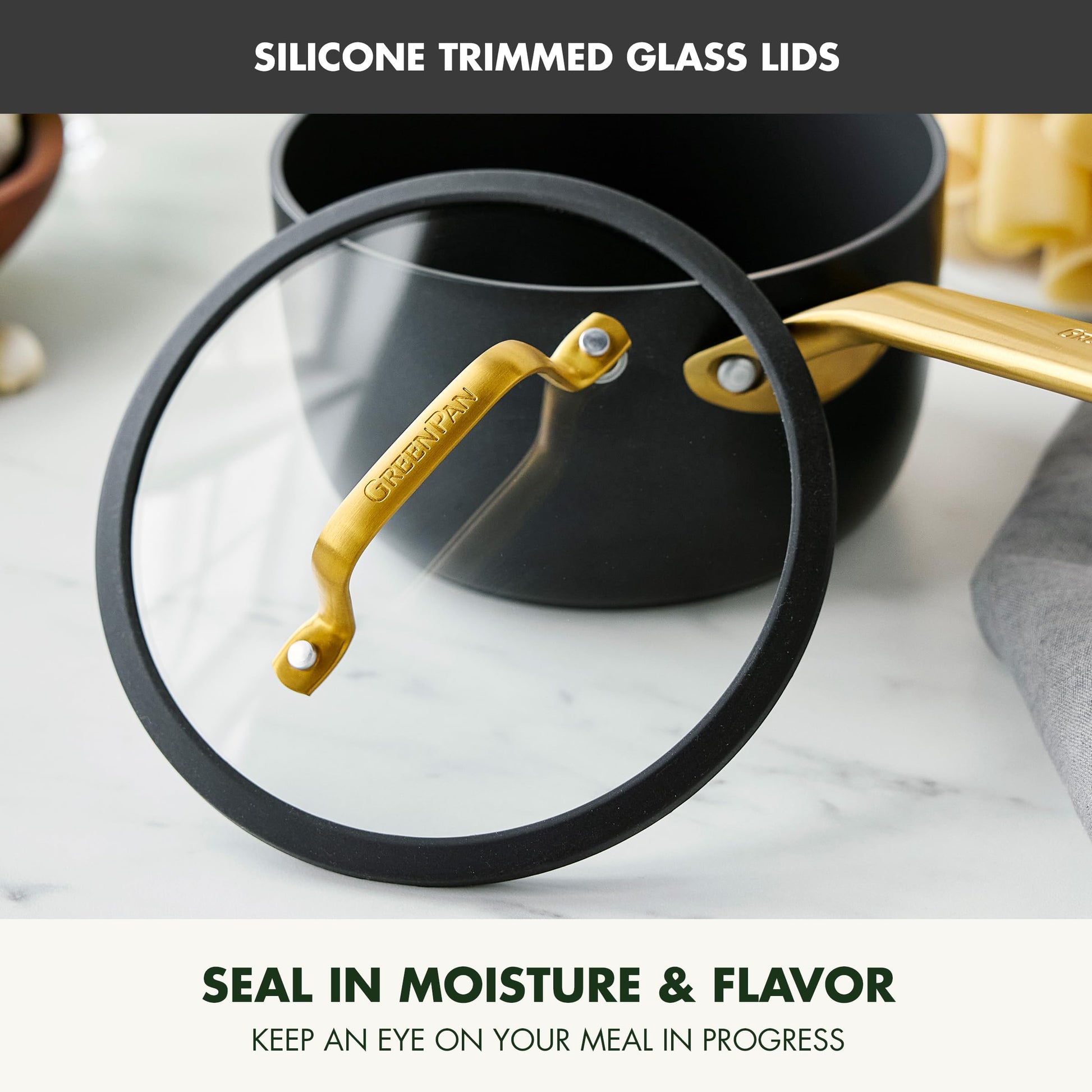 Glass lid with silicone trim on a pot, featuring gold handle, on a marble surface.