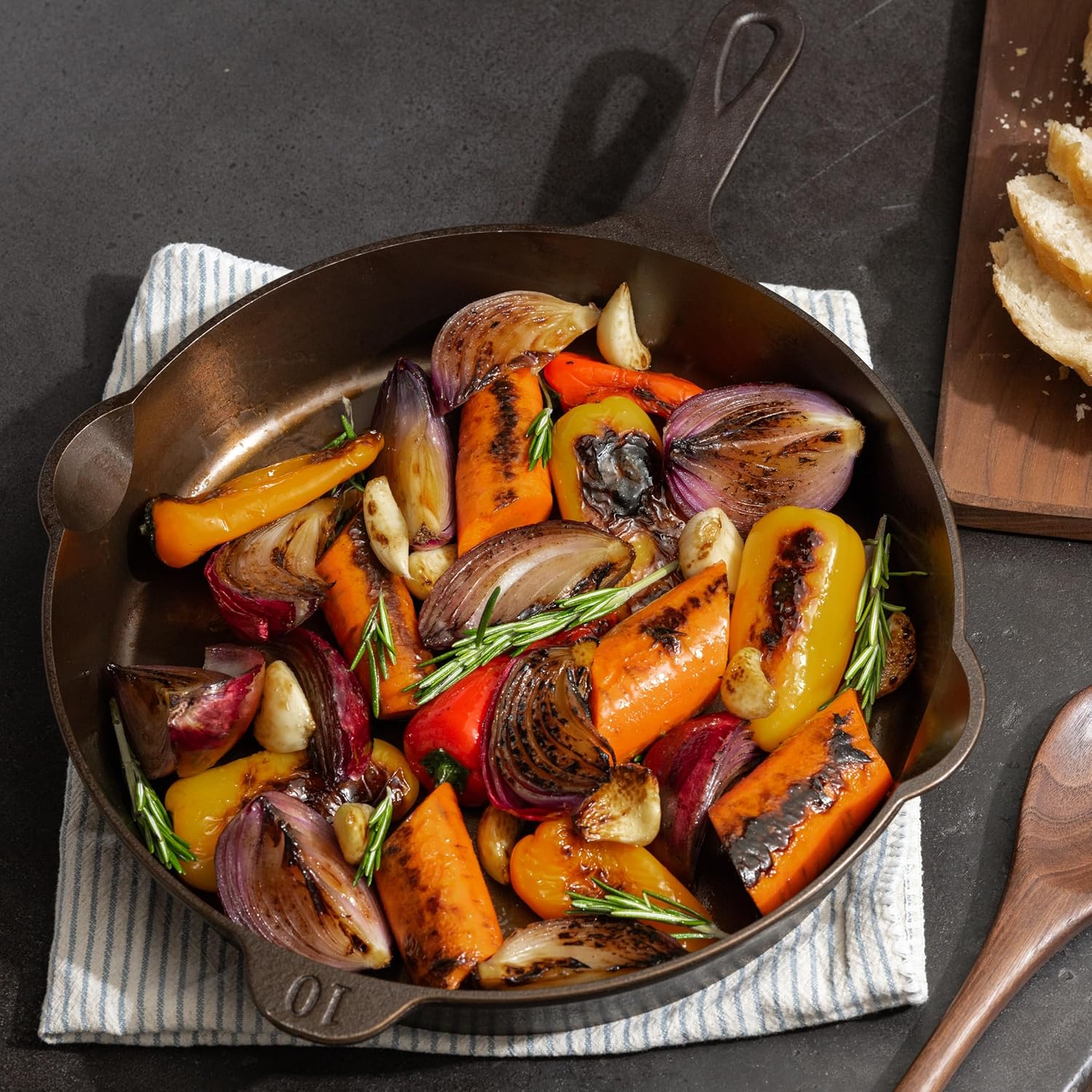 Roasted vegetables in a cast iron skillet on a dark surface with a wooden spoon.