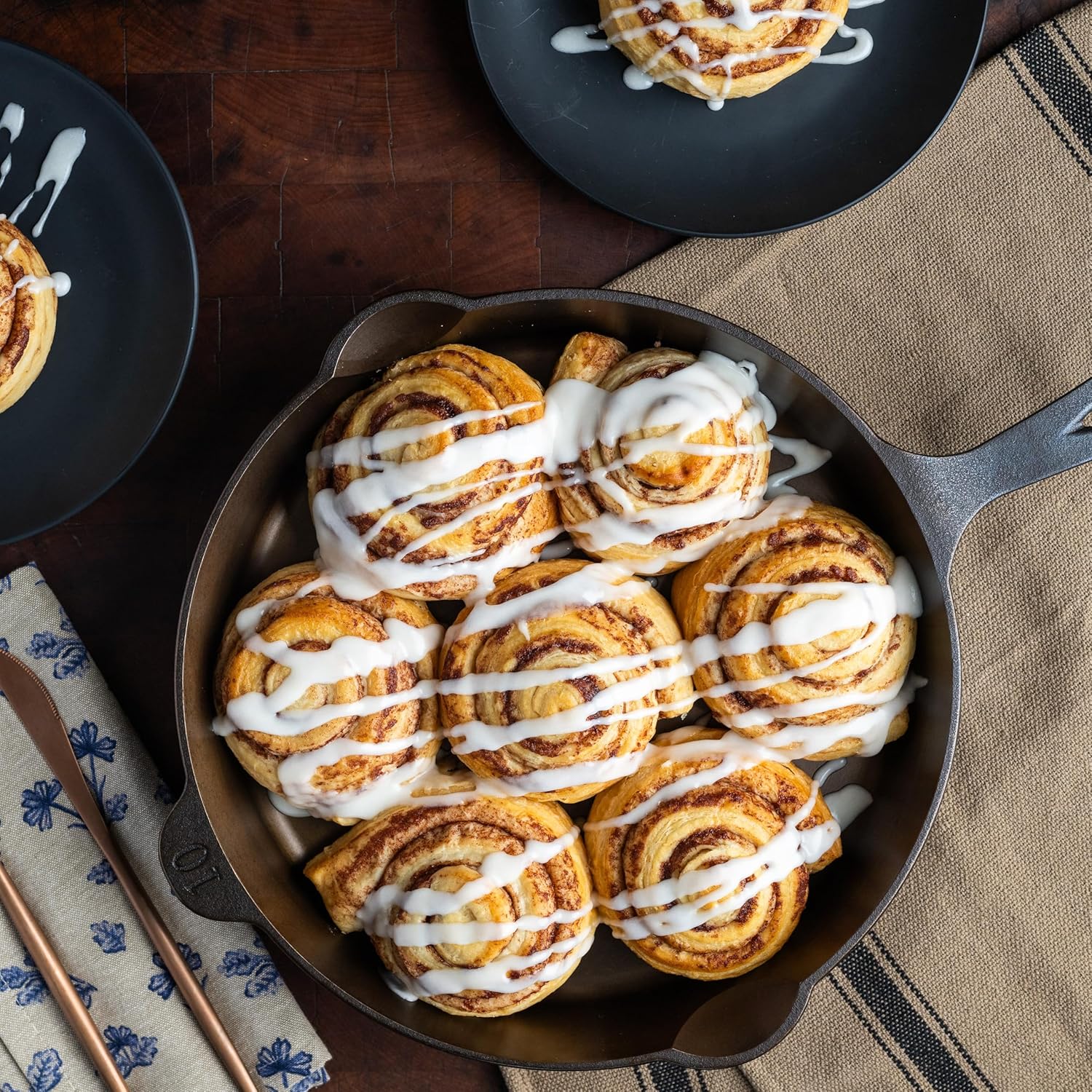 Cinnamon rolls with white icing in a cast iron skillet on a wooden table.