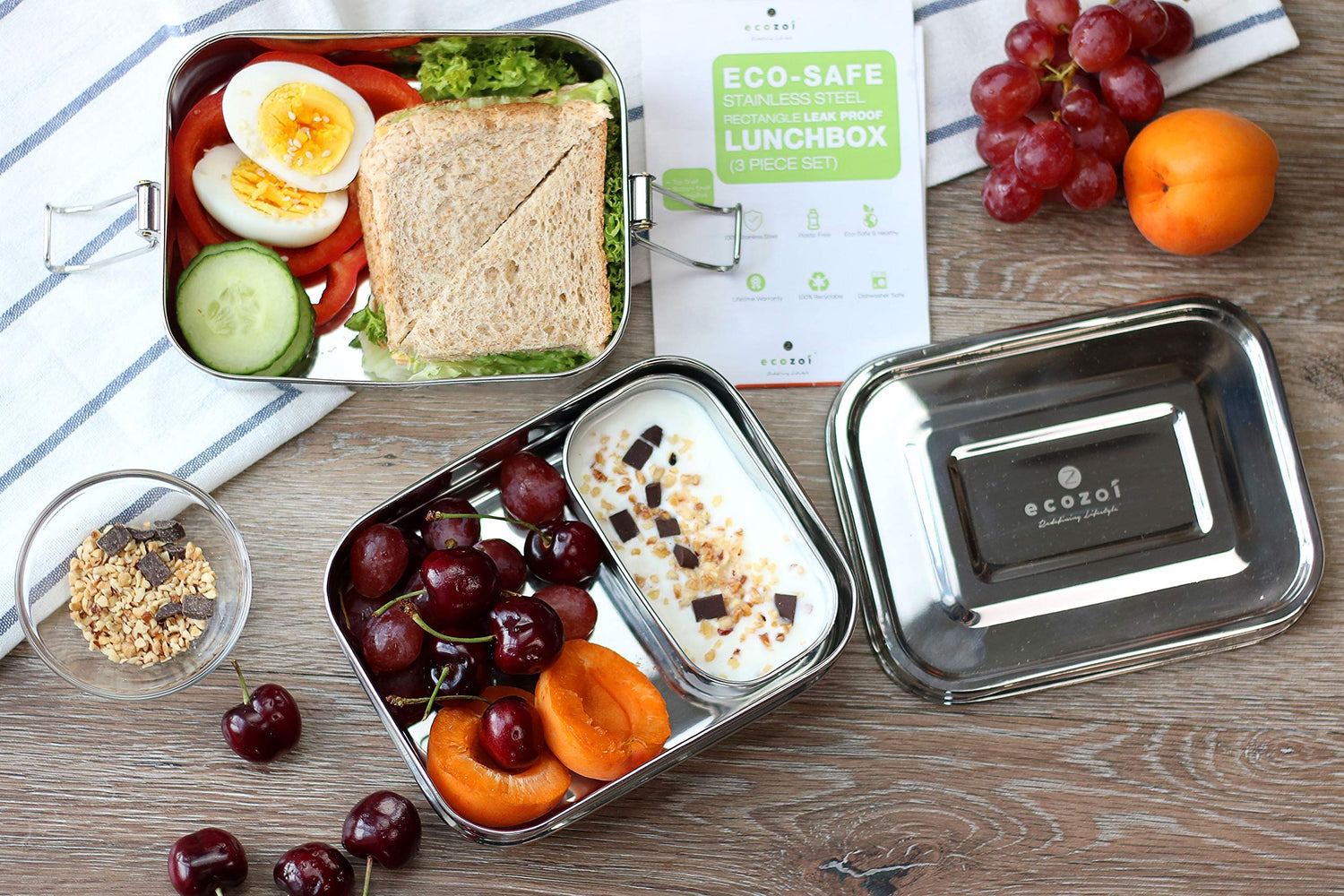 Metal lunch box with a sandwich, fruits, and a snack, next to an Eco-Safe lunchbox container.